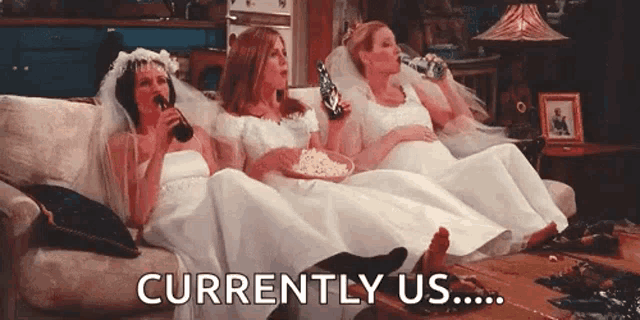 three brides are sitting on a couch drinking beer and eating popcorn .