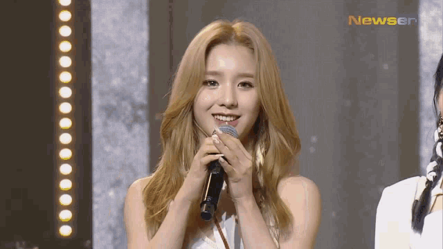 a woman is holding a microphone and smiling while standing on a stage .