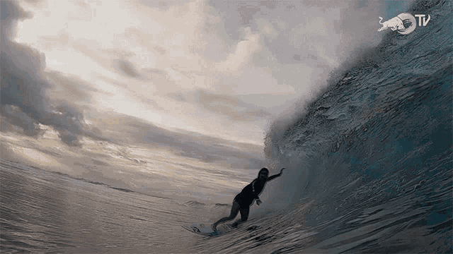 a surfer is riding a wave with a red bull tv logo behind him