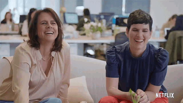 two women are sitting on a couch laughing with netflix written on the bottom