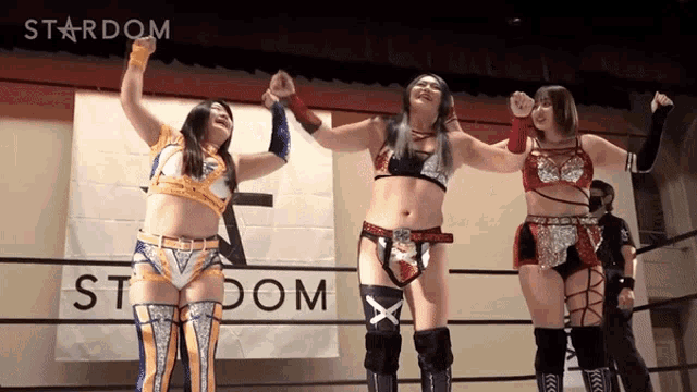 three female wrestlers are holding hands in front of a sign that says stardom