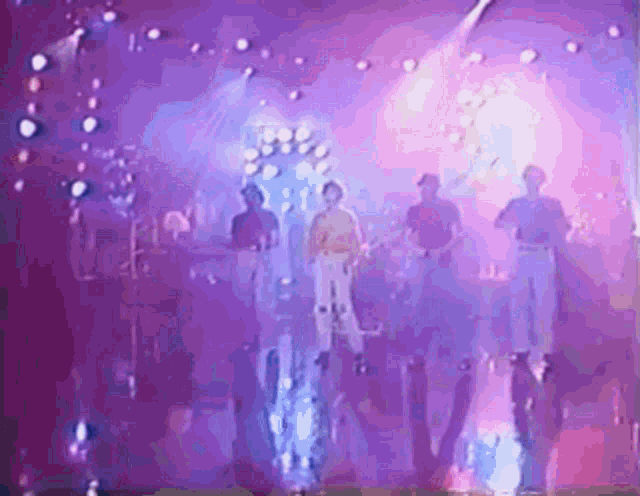 a group of people are standing on a stage in front of purple lights