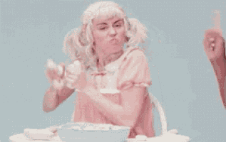 a woman in a pink dress is sitting at a table with a person pointing at her .