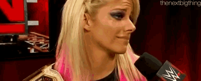 a woman is talking into a microphone while holding a wrestling championship belt .