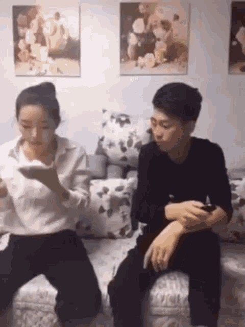 a man and a woman are sitting on a couch looking at their cell phones