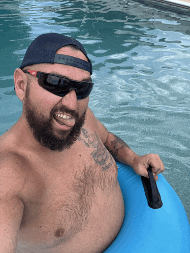 a shirtless man wearing sunglasses and a hat is floating on a blue tube in a pool