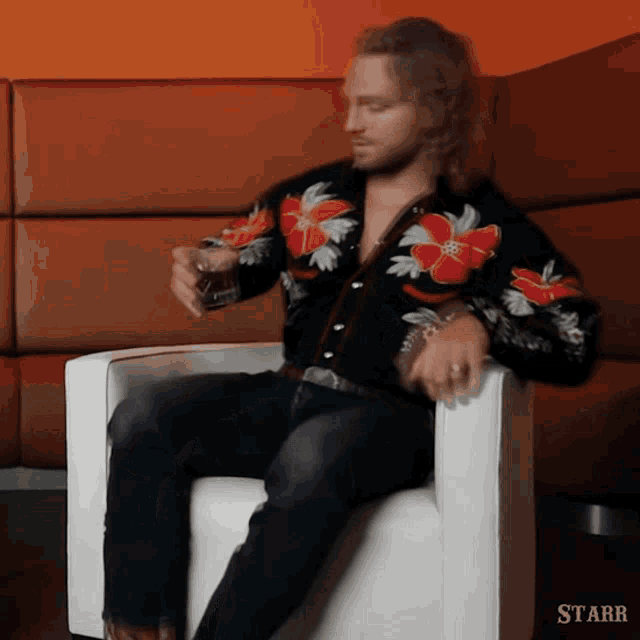 a man in a hawaiian shirt is sitting in a chair with a glass of whiskey in his hand