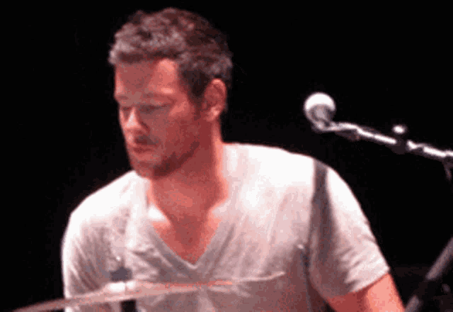 a man in a grey shirt is playing drums in front of a microphone
