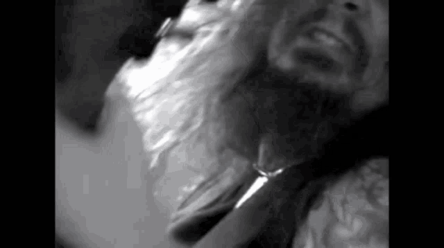 a black and white photo of a man with a beard and a necklace around his neck .