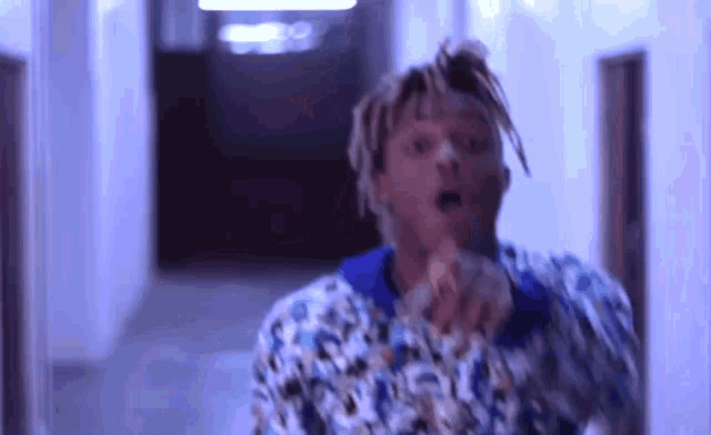 a man with dreadlocks is standing in a hallway with his mouth open and pointing at the camera .