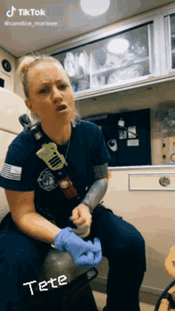 a female paramedic is sitting in an ambulance and talking to someone while wearing blue gloves .