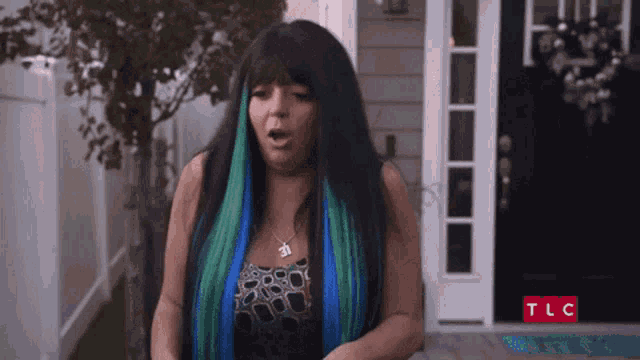 a woman with blue and green hair is standing in front of tlc