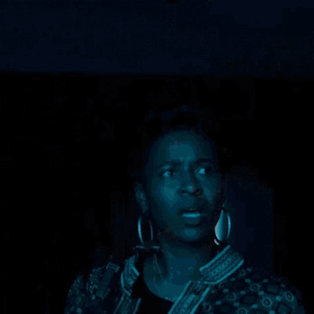 a woman wearing hoop earrings and a jacket looks surprised