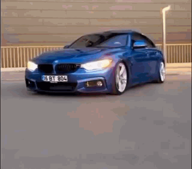 a blue bmw is driving down a street next to a fence .
