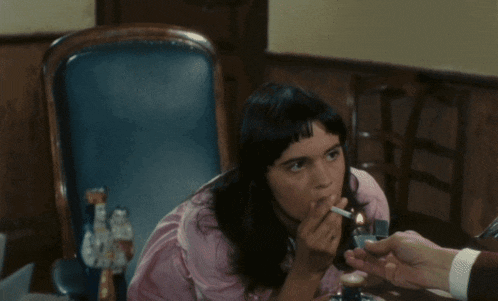 a woman in a pink shirt sits in a chair with smoke coming out of her mouth