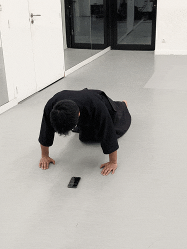 a man in a black kimono is doing push ups with a cell phone in front of him