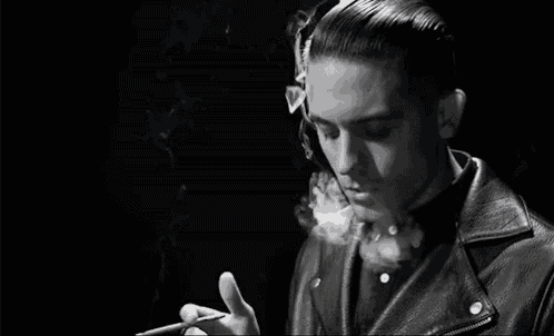 the man is wearing a leather jacket and smoking a cigarette .