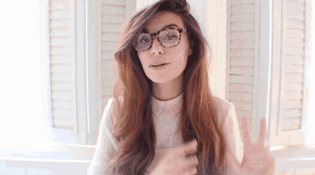 a woman wearing glasses and a white shirt is giving the peace sign