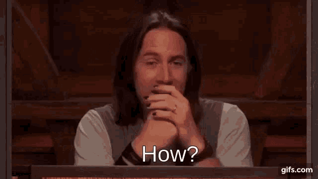 a man with long hair is laughing and covering his mouth with his hand .