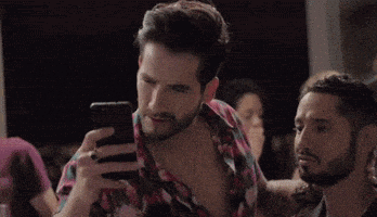 a man with a beard is looking at his cell phone in a crowded room .
