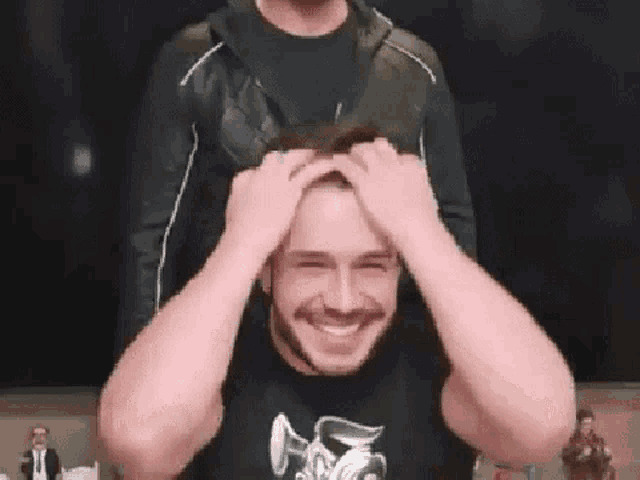 a man with a beard is smiling and holding his head while another man holds his head .