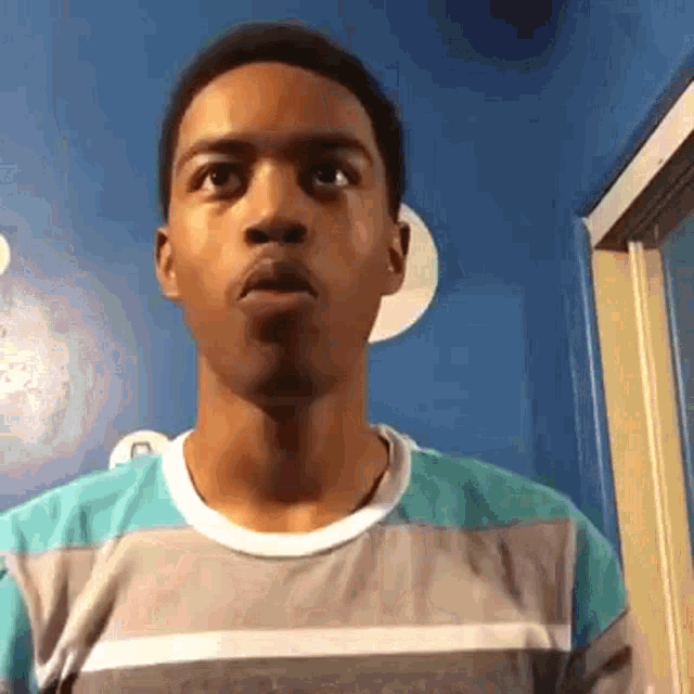 a young man wearing a striped shirt is standing in front of a blue wall .