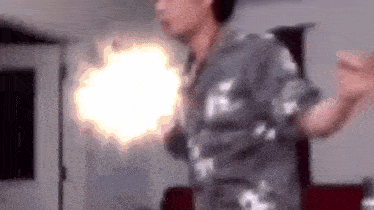 a man in a gray shirt is dancing in a room with a blurred background .