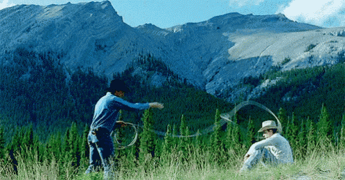 two men in cowboy hats are playing with a lasso in a field