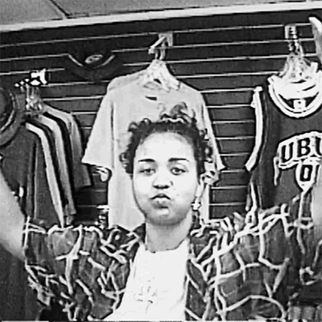 a black and white photo of a woman standing in front of a wall with clothes hanging on it .