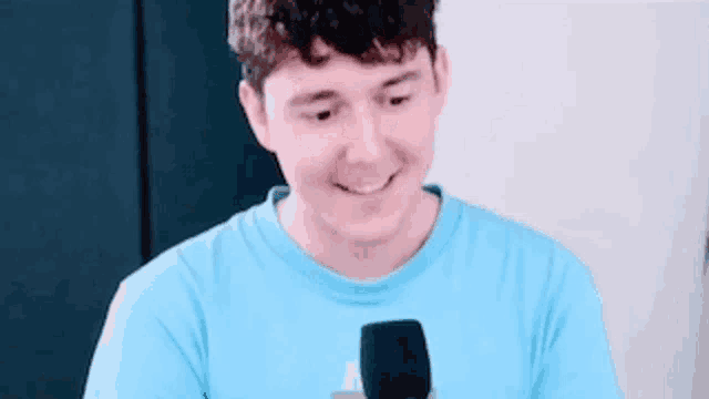 a young man in a blue shirt is smiling while holding a microphone .