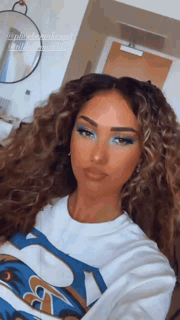 a woman with curly hair is wearing a white shirt with the letter a on the front