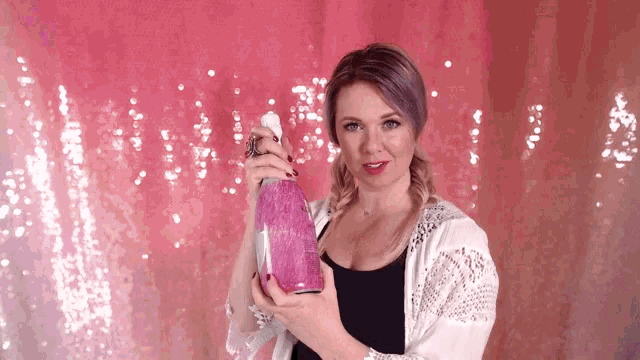 a woman is holding a pink bottle in front of a pink backdrop