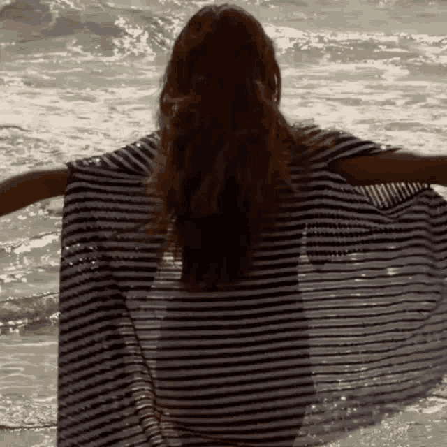 a woman in a striped dress is standing in the ocean with her arms outstretched