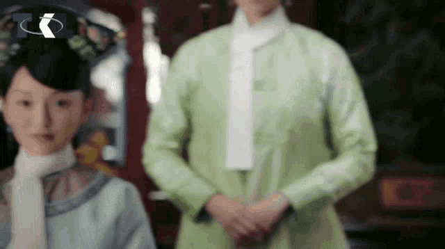 a woman in a green dress is standing next to another woman in a white scarf