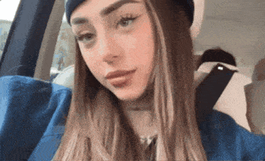 a woman wearing a beanie and a blue jacket is sitting in a car looking at the camera .