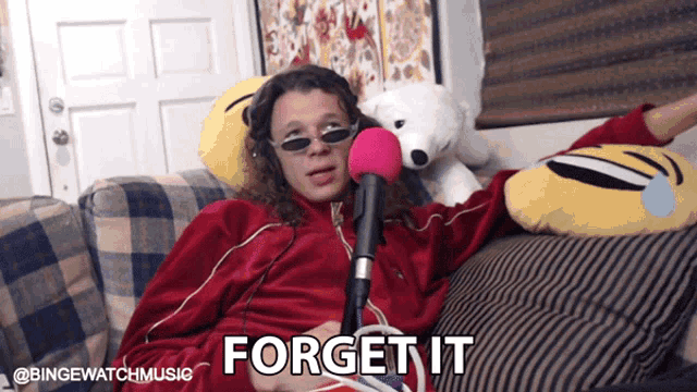 a man is sitting on a couch with a microphone and the words " forget it "