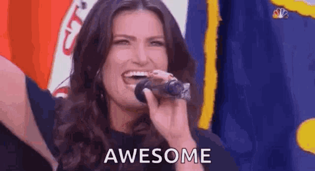 a woman is singing into a microphone and smiling while standing in front of a flag .