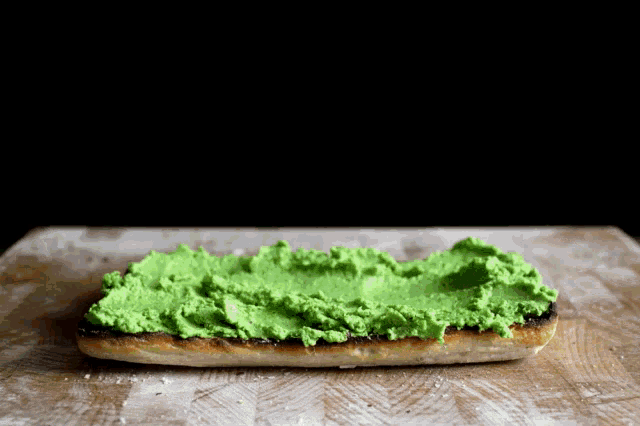 a piece of bread with green spread on it on a cutting board