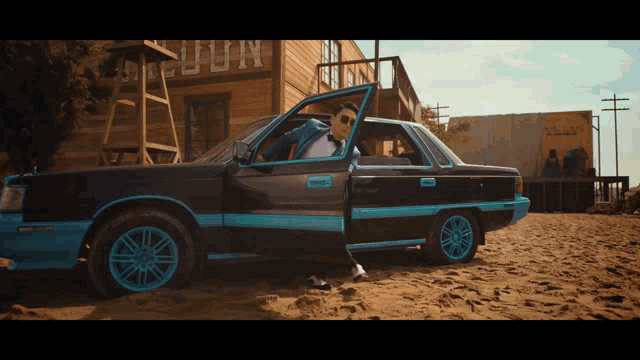 a man in a suit is getting out of a black car with blue rims