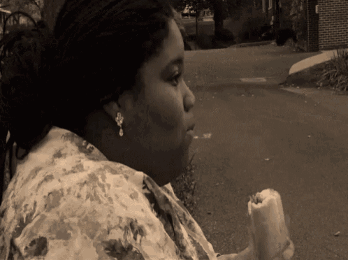 a woman in a floral shirt holds a hot dog in her hand