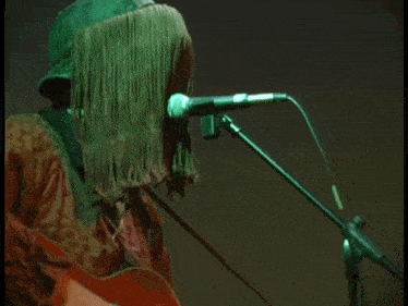 a person with a fringed hat on playing a guitar and singing into a microphone