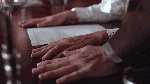 a man and woman are sitting at a table with their hands on a piece of paper .