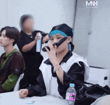 a man is sitting at a table with a bottle of water in front of him and a sign that says mh on it