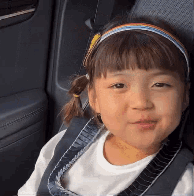 a little girl wearing a rainbow headband is sitting in the back seat of a car