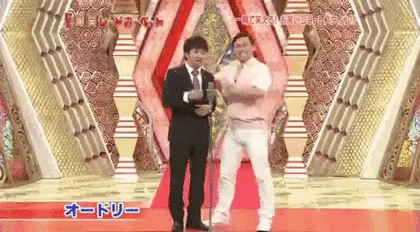 two men are standing next to each other on a red carpet in front of a stage .