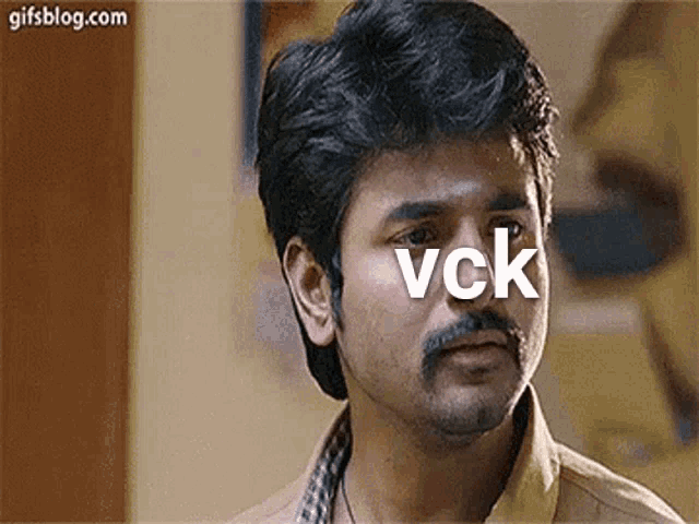 a man with a beard and mustache is looking at the camera with the word vck written on his face .