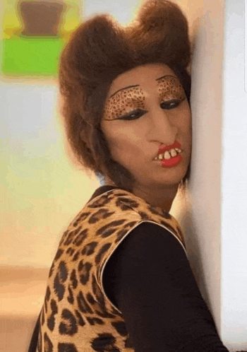 a woman wearing a leopard print vest and a wig is leaning against a wall .