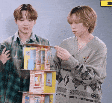 two young men standing next to each other looking at a stack of houses