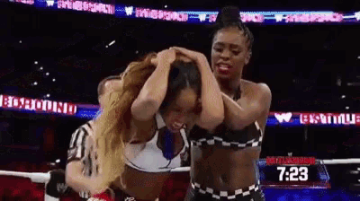 two women are fighting in a boxing ring while a referee looks on .