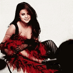 a woman in a red feathered dress is sitting on the floor